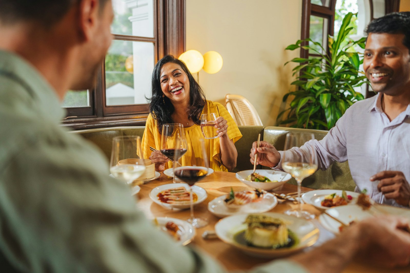 Friends laughing around a restaurant table, glasses of wine in hand